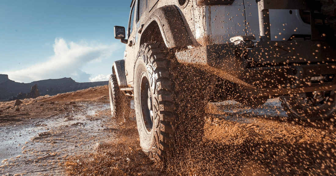 A rugged off-road Jeep kicking up mud while driving through a wet dirt trail in the desert