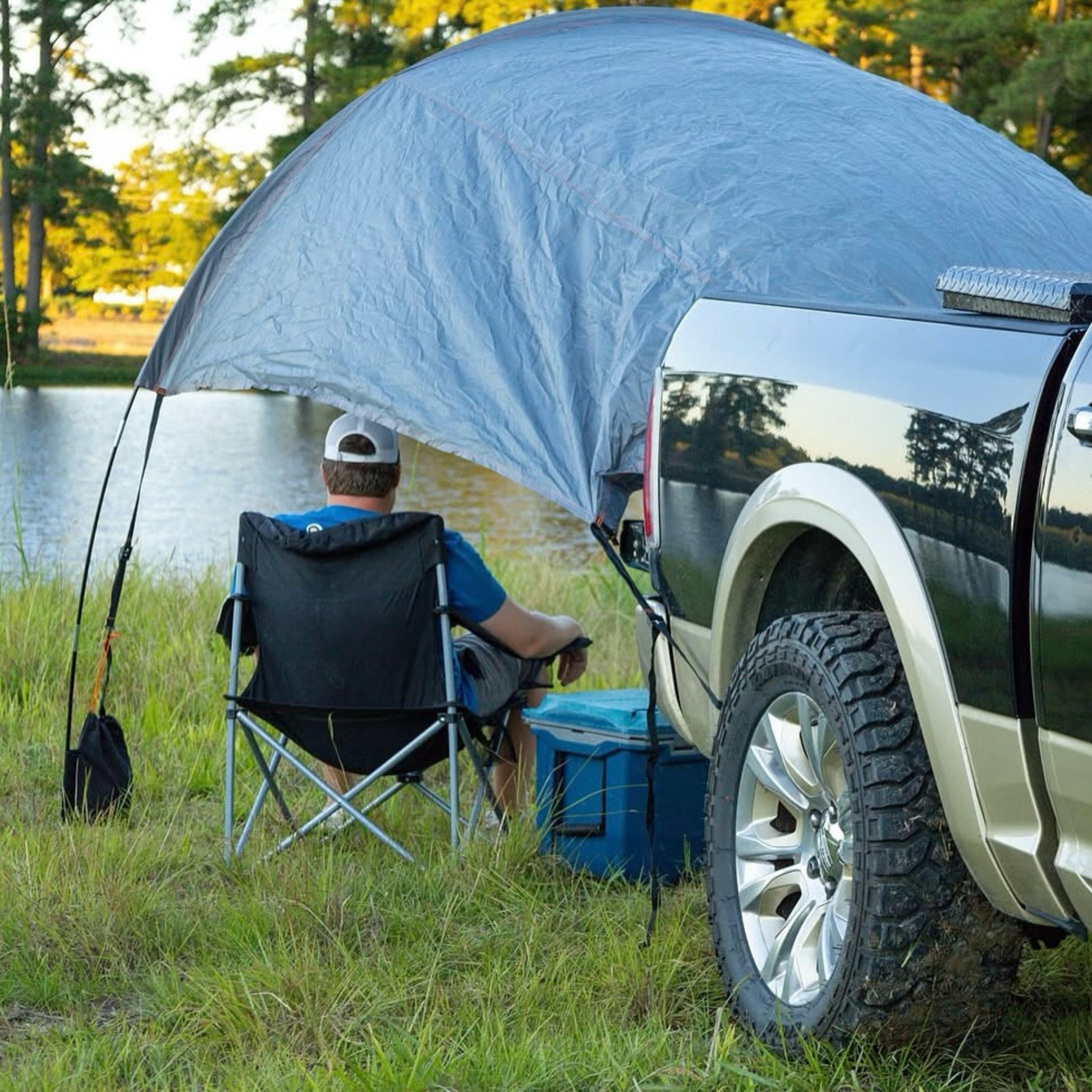 Trail Gear Oasis truck sun shade deployed at lakeside camping spot with person relaxing in chair under canopy